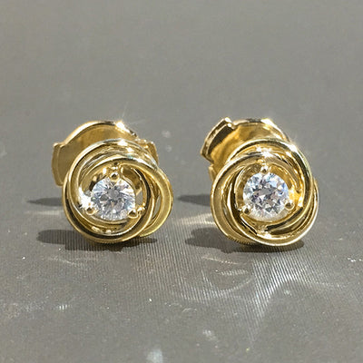 Pair gold swirl knot clear CZ studs front view on grey surface
