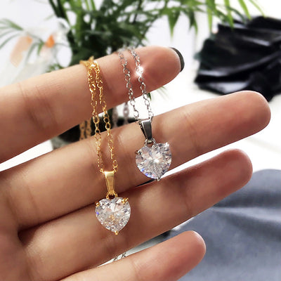 Hand holding gold and silver heart clear CZ pendant necklaces side by side