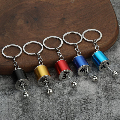 Five colored gear shift lever keychains arranged on a wooden board.