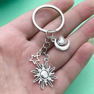 A silver-tone sun, crescent moon, heart, and outline star keychain rests on a hand.