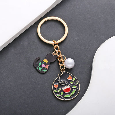 Front product photo of black cat flower and pearl enamel charm keychain with round ring showing the pictured design arra