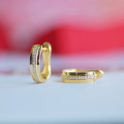 Gold crystal channel huggie hoops on white surface with red blurred backdrop