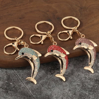 Three gold-tone dolphin keychains with blue, red, and purple rhinestones displayed on wood.