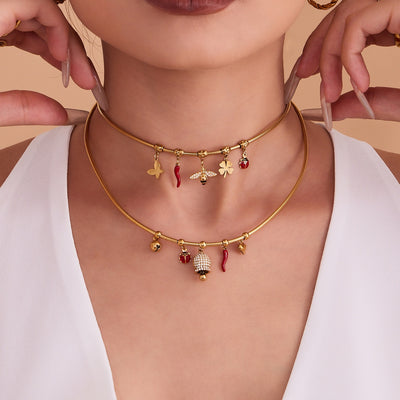 Model wearing layered gold snake chain charm necklaces with bee and bell