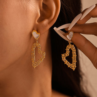 Gold woven heart drop earrings with white shell studs on model