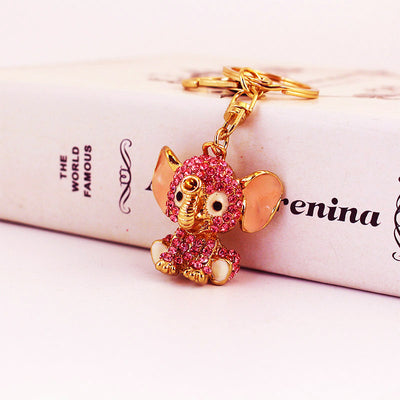 Angled front view of a pink rhinestone elephant charm beside a printed box.