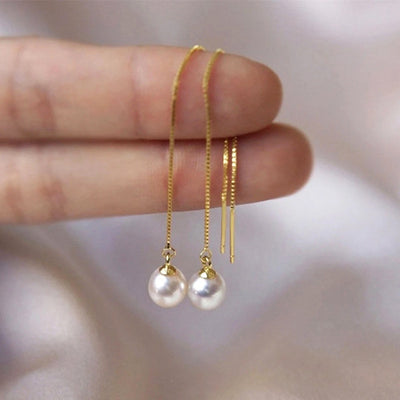 Gold threader earrings with white pearl drops held between fingers