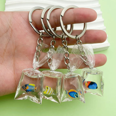 Four clear bag-shaped tropical fish keychains rest across a person's hand.