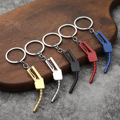 Five gas pump nozzle keychains in gold tone, silver tone, black, red, and blue arranged on a wooden board.