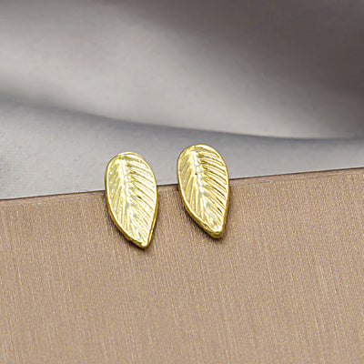 Pair of gold textured leaf stud earrings on beige fabric surface