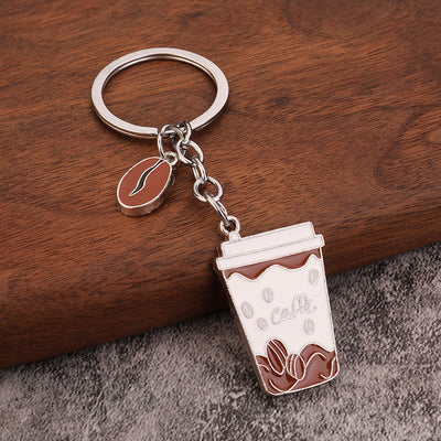 A silver-tone key ring holds a brown and white cafe cup pendant and bean charm on a wooden surface.