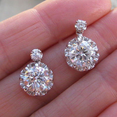 Silver-tone round solitaire halo drop earrings held on a palm