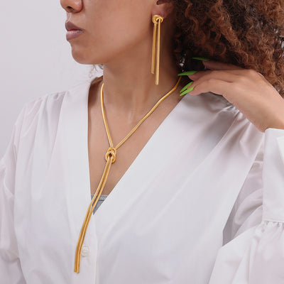 Model in white shirt wearing gold knot snake lariat necklace and tassel earrings