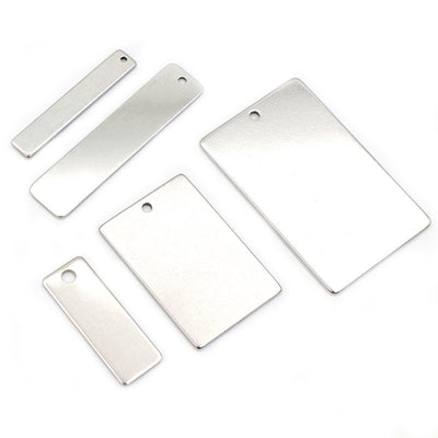 Front overview of polished rectangular metal tag blanks with single holes arranged on a light background