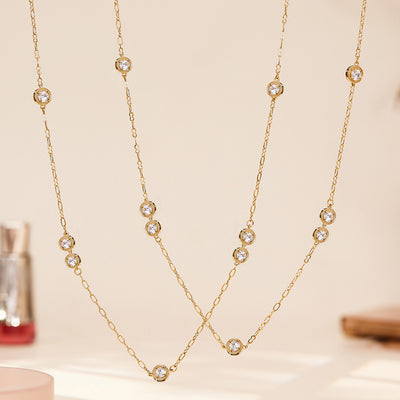 Two gold long zircon station necklaces hanging crossed on beige backdrop