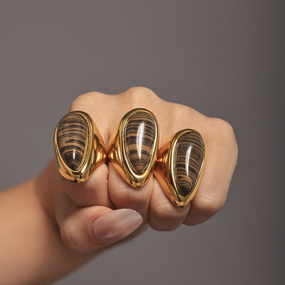 Fist wearing three gold teardrop wood grain stone dome rings