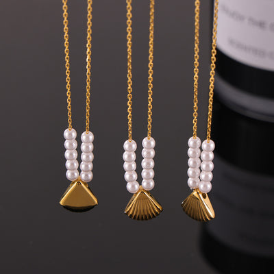 Three gold shell pendant necklaces with pearl beads on dark surface