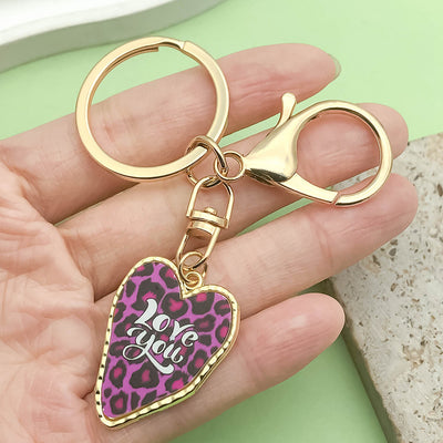 Image 1 showing a person holding up a pink and black heart shaped keychain.