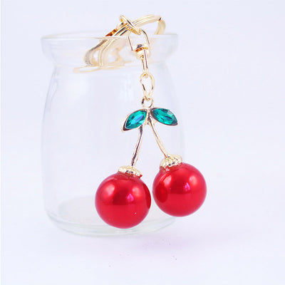 Red cherry keychain hanging from the rim of a clear glass jar.