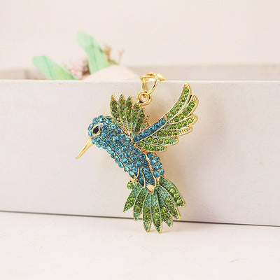 A blue and green stone-studded hummingbird charm hangs against a pale display.