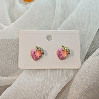 Pair of pink peach heart enamel stud earrings on white card over tulle