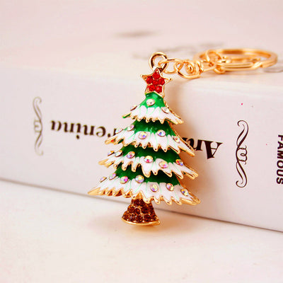 Front view of a green and white rhinestone Christmas tree charm resting on a book beside its key ring.