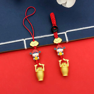 Two red cord ornaments with deity, cloud and gold-tone bucket details rest beside a blue book.