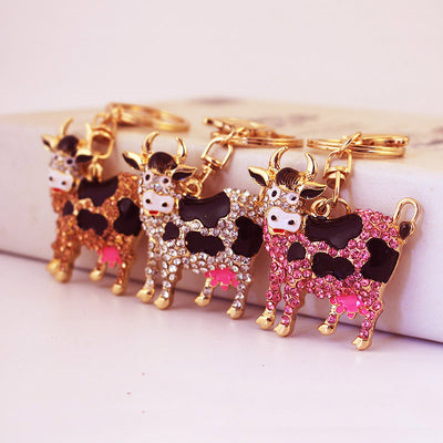 Three rhinestone cow keychains in peach, white and pink arranged side by side.
