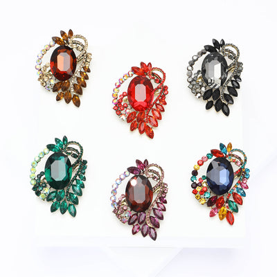 An oval faceted stone framed by leaf-like crystals and a bow shown on a white background