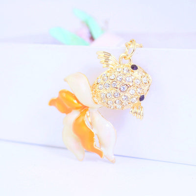 Side view of a gold-tone goldfish charm with clear stones and an orange and white tail.