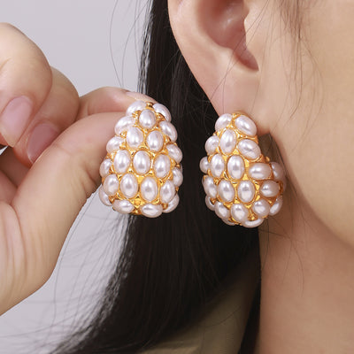 Model holding gold teardrop pearl cluster earring beside ear