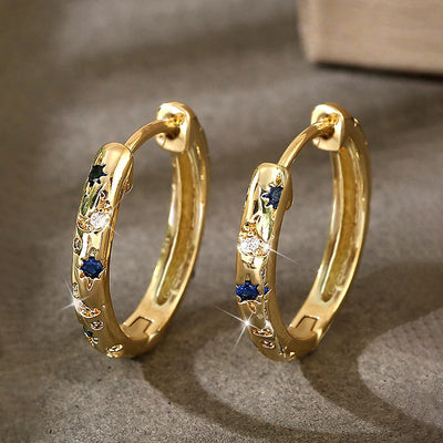 Pair of gold star moon blue stone huggie hoops on grey stone surface