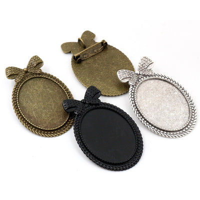 Overview of oval bezel settings with bow tops and pin clasps on the back on a light background