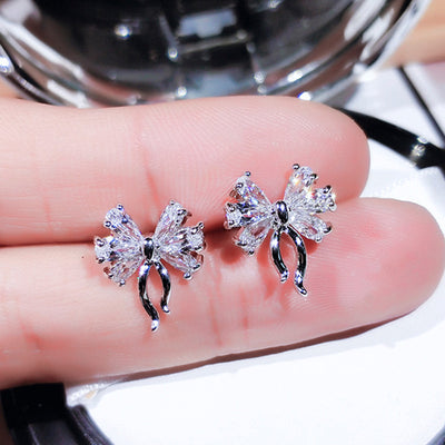 Silver bow clear stud earrings held between fingers close-up