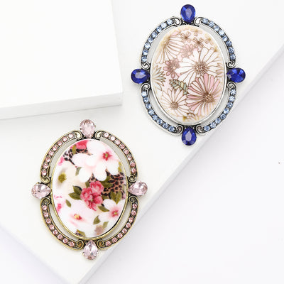 An oval floral cameo framed by crystals and colored accents shown on a white background