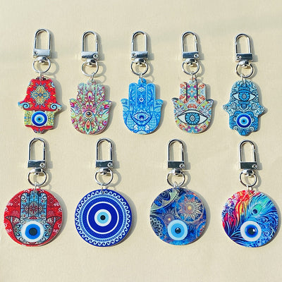 Nine hamsa and evil eye print keychains with silver clasps on beige surface