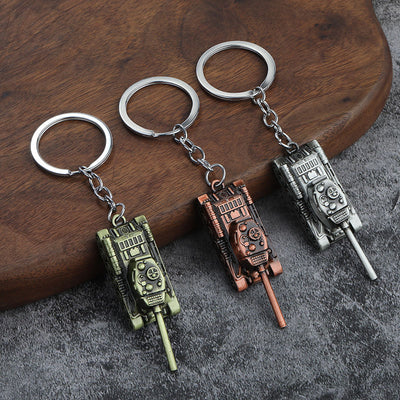 Three tank model keychains in antique bronze, copper, and silver finishes on a wooden surface.