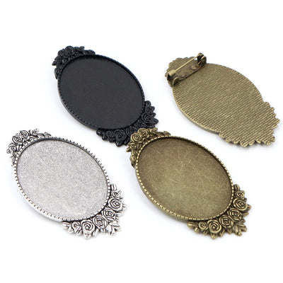 Oval cabochon brooch tray with floral edging and a pin back in a group view on a white background