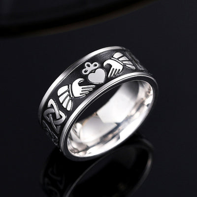 Steel Claddagh band ring on black reflective surface showing heart hands