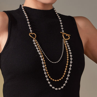 Model wearing multi-layer two-tone ball chain necklace with gold heart toggle