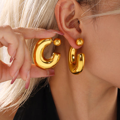 Gold C hollow hoop earrings with ball posts worn and held by model