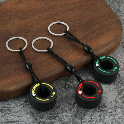 Three black tire keychains display yellow, red, and green raised accents on a wood surface.