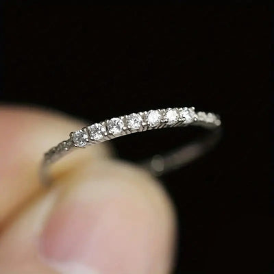 White gold thin half eternity CZ band ring held between fingers