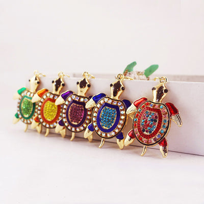 Five gold-tone turtle pendants in green, orange, purple, blue, and red are arranged in a row.
