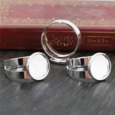 Overview of silver-tone adjustable ring blanks with smooth round bezel pads on a light background