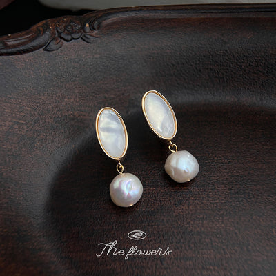 Gold oval shell pearl drop earrings on dark carved wood tray