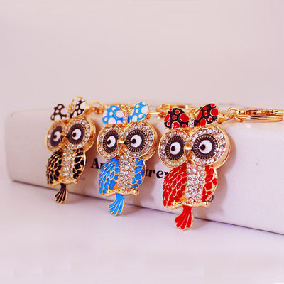 Three owl keychains in black, blue, and red displayed side by side.