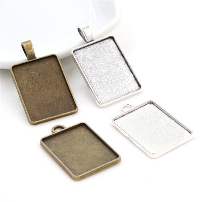 Assorted rectangular pendant bezel trays in silver and bronze tones arranged together on a plain background