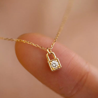 Mini gold lock pendant necklace held on fingertip