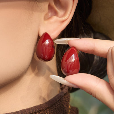 On-ear view of glossy burgundy teardrop stud earrings in main image 1.